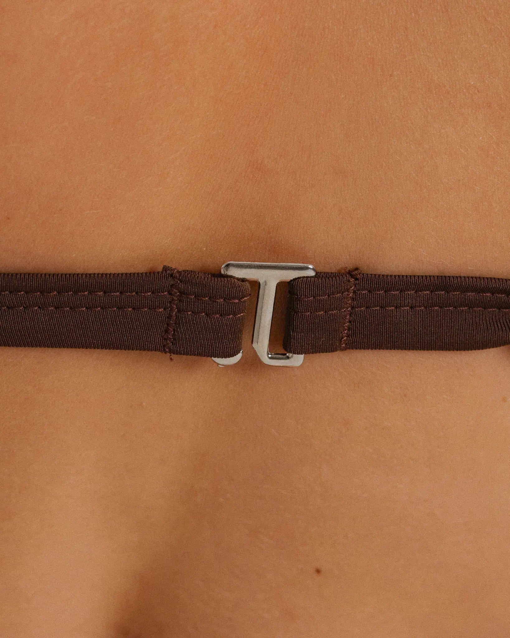 Gros plan du fermoir métallique au dos d’un haut de bikini marron avec bretelles ajustables